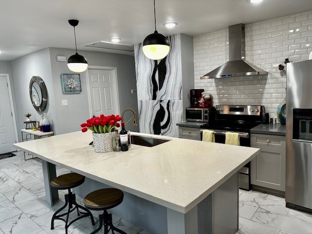 kitchen featuring sink, hanging light fixtures, stainless steel appliances, wall chimney exhaust hood, and a center island with sink