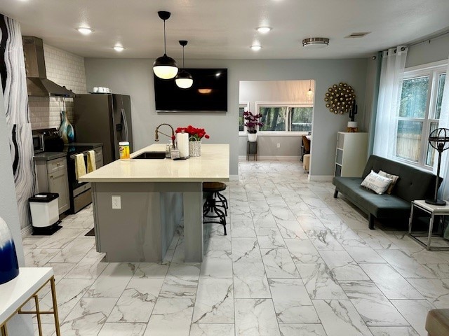 kitchen with appliances with stainless steel finishes, sink, wall chimney exhaust hood, decorative light fixtures, and a center island with sink