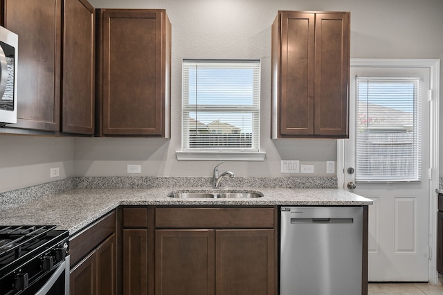 kitchen featuring appliances with stainless steel finishes, sink, dark brown cabinets, and light stone counters