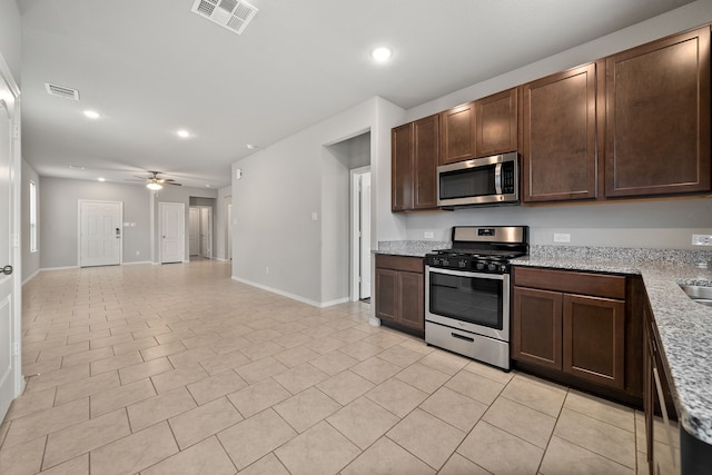 kitchen with light stone countertops, stainless steel appliances, dark brown cabinets, and ceiling fan