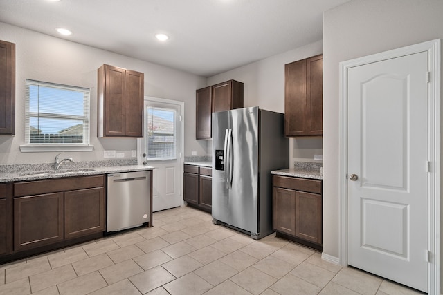 kitchen featuring appliances with stainless steel finishes, light stone countertops, sink, and dark brown cabinets