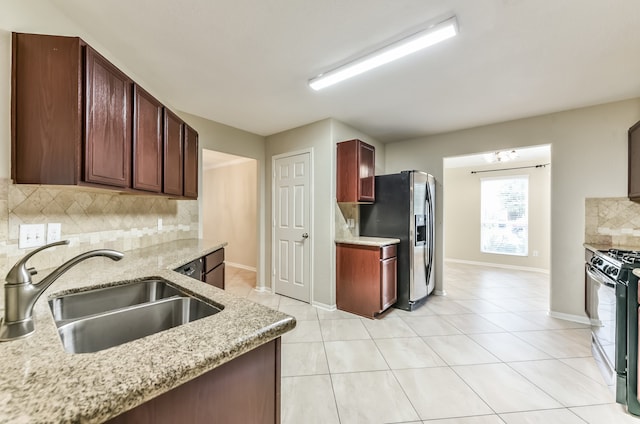 kitchen with gas range, sink, light stone countertops, stainless steel fridge with ice dispenser, and tasteful backsplash