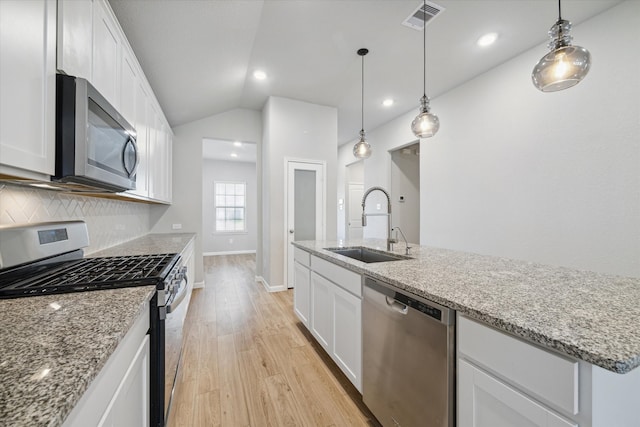 kitchen featuring appliances with stainless steel finishes, backsplash, vaulted ceiling, white cabinets, and a kitchen island with sink