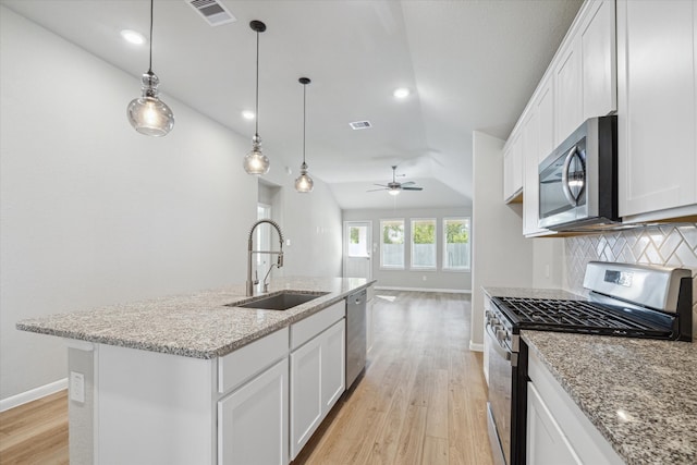 kitchen with lofted ceiling, an island with sink, white cabinetry, sink, and stainless steel appliances