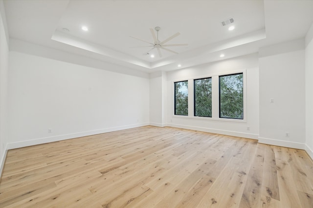 spare room with a tray ceiling and light hardwood / wood-style floors