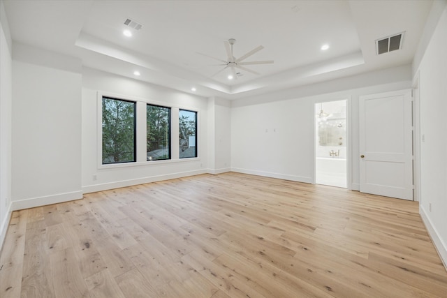 unfurnished room with ceiling fan, light wood-type flooring, and a tray ceiling