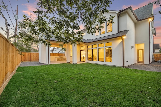 back house at dusk with a lawn and a patio area