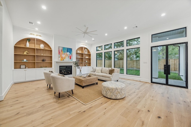 living room with built in shelves, light hardwood / wood-style floors, and ceiling fan