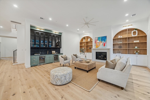 living room featuring bar, wine cooler, built in features, and light wood-type flooring