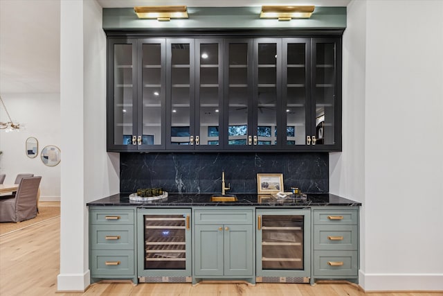 bar featuring decorative backsplash, light hardwood / wood-style floors, beverage cooler, and dark stone counters