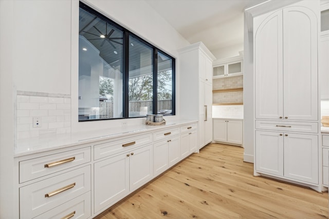 bar with decorative backsplash, light hardwood / wood-style floors, and white cabinetry