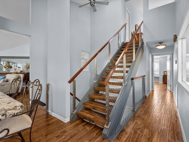 staircase with a high ceiling, hardwood / wood-style floors, ceiling fan, and plenty of natural light