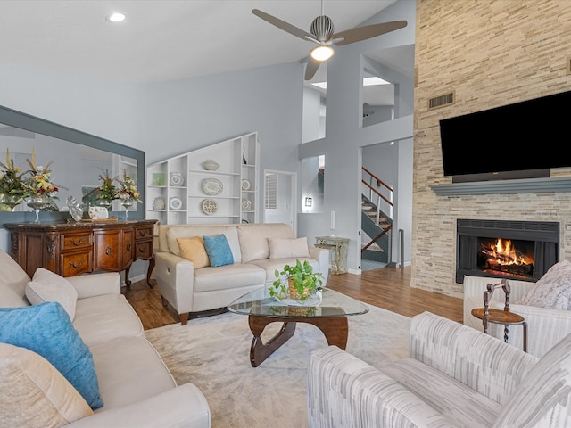 living room with light hardwood / wood-style floors, ceiling fan, high vaulted ceiling, a fireplace, and built in features