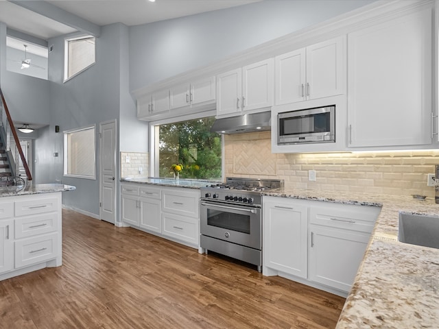 kitchen with white cabinets, light stone countertops, light wood-type flooring, and appliances with stainless steel finishes