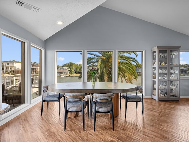 dining room featuring a wealth of natural light, wood-type flooring, a water view, and high vaulted ceiling