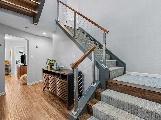 stairs featuring wood-type flooring and beamed ceiling