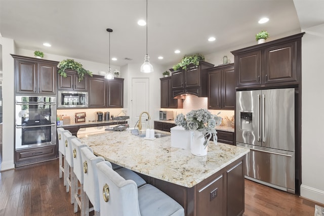 kitchen featuring tasteful backsplash, an island with sink, dark hardwood / wood-style flooring, stainless steel appliances, and pendant lighting