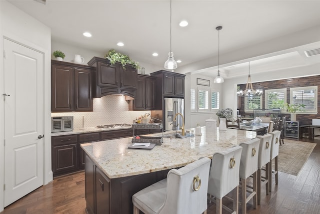 kitchen featuring a large island with sink, appliances with stainless steel finishes, a kitchen breakfast bar, hanging light fixtures, and dark wood-type flooring