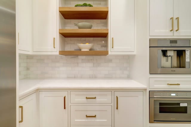 kitchen with oven, decorative backsplash, white cabinets, and light stone countertops