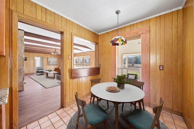 dining room with ornamental molding, wooden walls, a textured ceiling, and light hardwood / wood-style floors