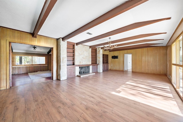 unfurnished living room featuring beam ceiling, light hardwood / wood-style flooring, a notable chandelier, and wood walls