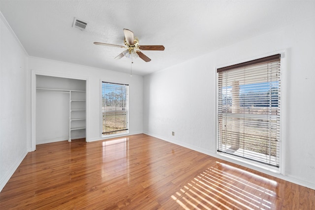 unfurnished bedroom with ceiling fan, hardwood / wood-style flooring, a textured ceiling, and multiple windows