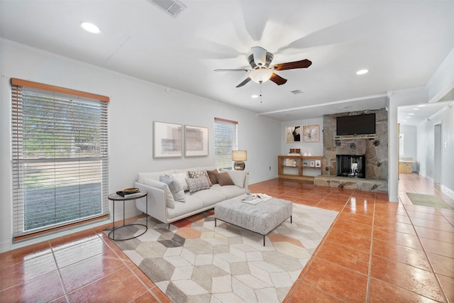 living room with ceiling fan, a stone fireplace, ornamental molding, and tile patterned flooring