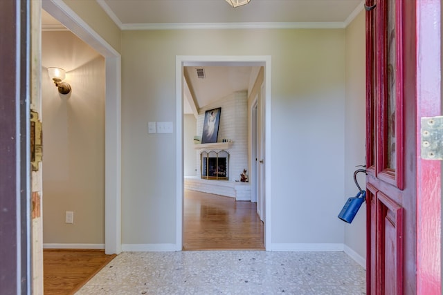 foyer entrance featuring light hardwood / wood-style floors, ornamental molding, vaulted ceiling, and a brick fireplace