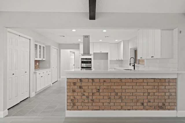 kitchen with decorative backsplash, white cabinets, wall chimney exhaust hood, sink, and stainless steel double oven