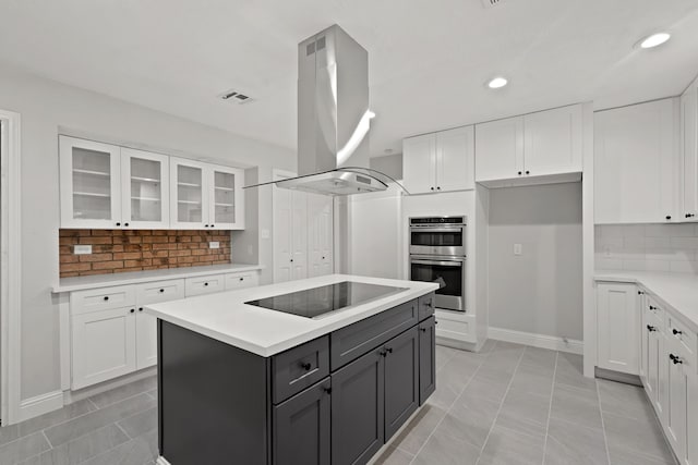 kitchen with black electric stovetop, island exhaust hood, tasteful backsplash, and white cabinetry