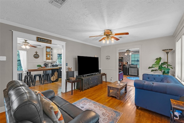 living room featuring crown molding, wood-type flooring, a textured ceiling, and ceiling fan