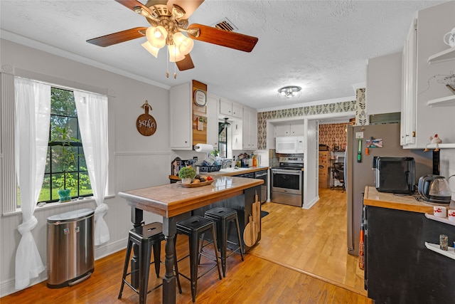 kitchen with light hardwood / wood-style flooring, stainless steel appliances, ornamental molding, white cabinets, and ceiling fan