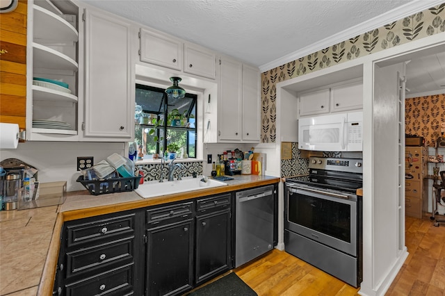 kitchen with appliances with stainless steel finishes, sink, white cabinets, ornamental molding, and light hardwood / wood-style flooring