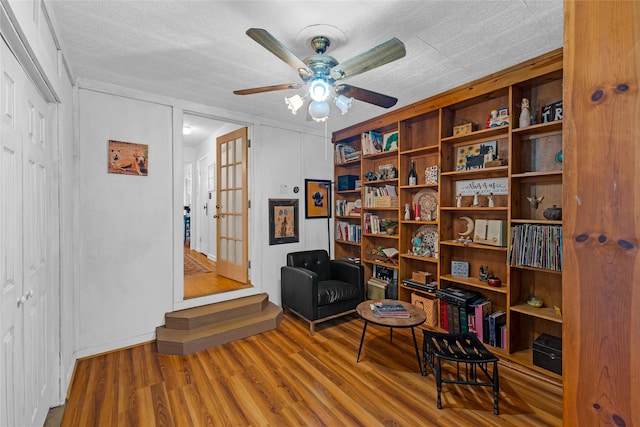 living area featuring ceiling fan, wood-type flooring, and a textured ceiling