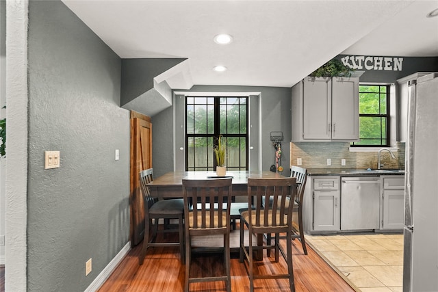 kitchen with stainless steel dishwasher, backsplash, light hardwood / wood-style floors, and gray cabinets