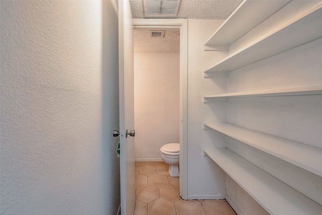 bathroom with toilet, a textured ceiling, and tile patterned flooring