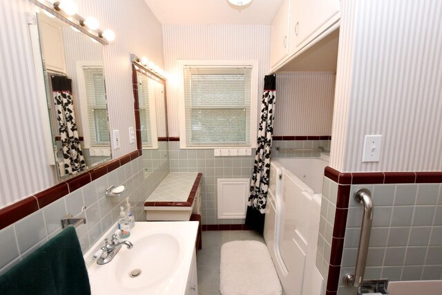 bathroom featuring vanity, a bath, and tile walls