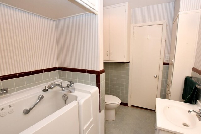 bathroom featuring vanity, a tub to relax in, toilet, and tile walls