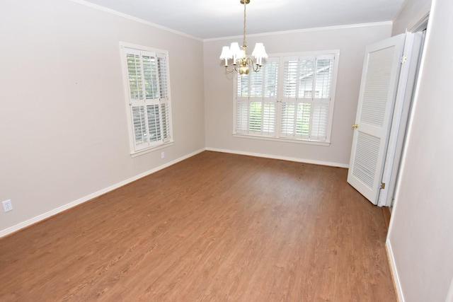 empty room with hardwood / wood-style floors, crown molding, plenty of natural light, and a chandelier