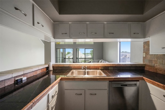 kitchen featuring white cabinets, sink, stainless steel dishwasher, decorative backsplash, and tile counters