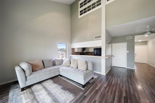 living room with ceiling fan, a towering ceiling, and dark wood-type flooring