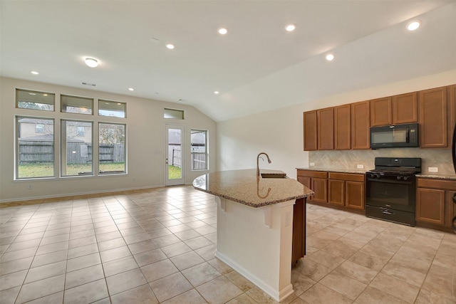 kitchen with tasteful backsplash, light stone counters, vaulted ceiling, a kitchen island with sink, and black appliances