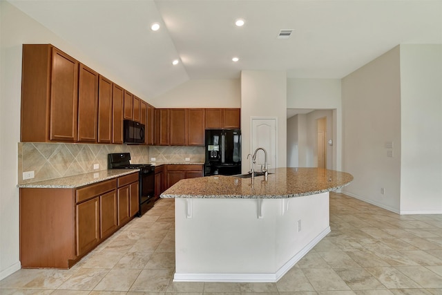 kitchen with lofted ceiling, a kitchen island with sink, black appliances, sink, and light stone countertops