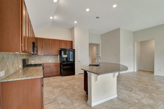 kitchen featuring stone counters, sink, black refrigerator with ice dispenser, lofted ceiling, and a kitchen island with sink