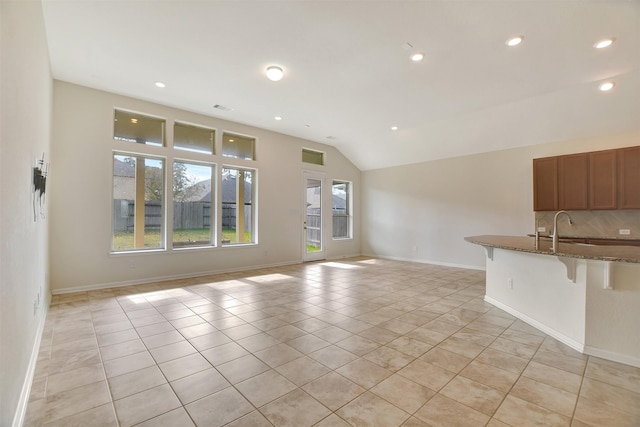 unfurnished living room featuring light tile patterned floors, vaulted ceiling, and sink