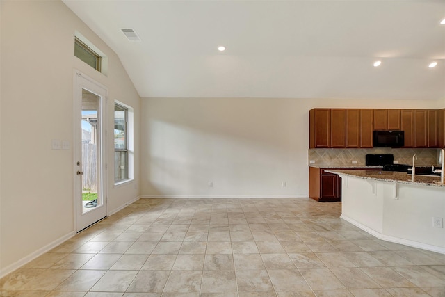 kitchen featuring backsplash, black appliances, vaulted ceiling, light stone countertops, and a kitchen bar