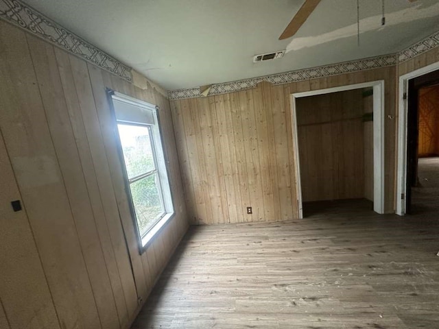 unfurnished bedroom with ceiling fan, light hardwood / wood-style floors, and wood walls