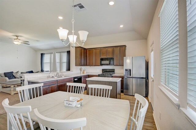 kitchen with black appliances, sink, ceiling fan with notable chandelier, lofted ceiling, and pendant lighting