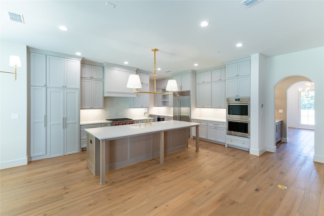 kitchen with stainless steel appliances, a center island with sink, a breakfast bar, pendant lighting, and light hardwood / wood-style floors