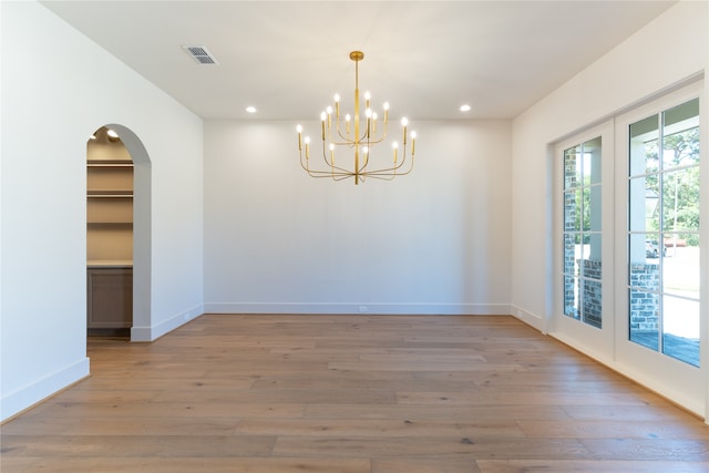 spare room featuring french doors, a chandelier, and hardwood / wood-style floors